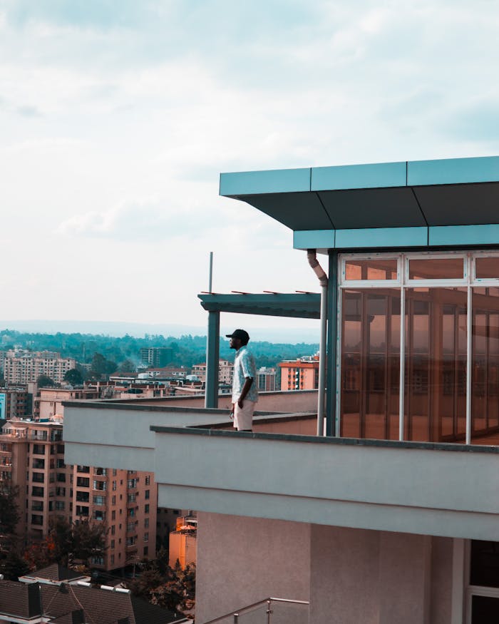 Man standing on a modern balcony overlooking a city skyline on a bright day.